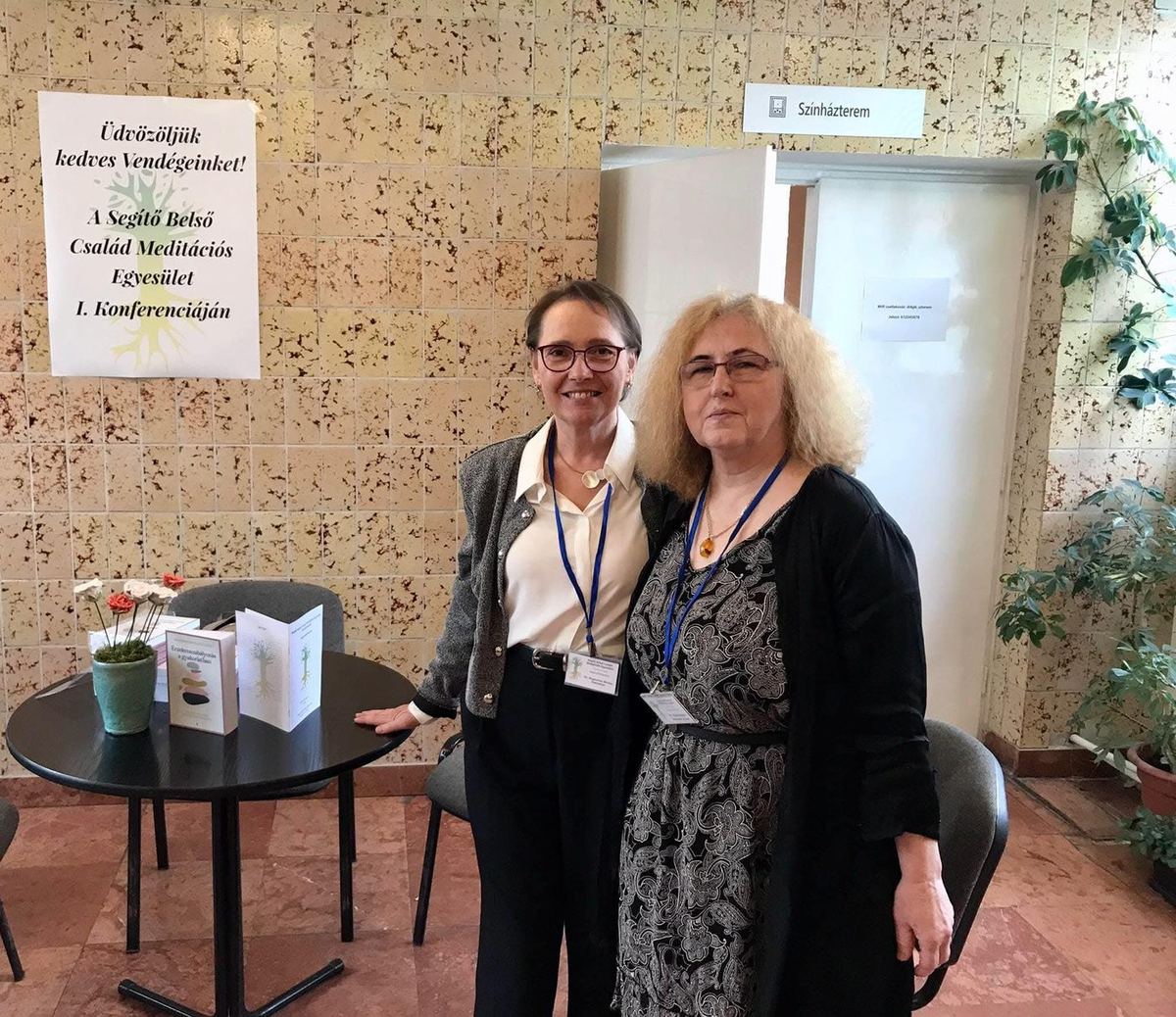 A konferencia két nyitó előadója a művelődési ház aulájában, mellettük az egyesület köszöntő plakátja.